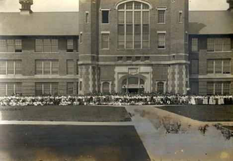 Students, along with faculty and staff, gather outside the front entrance of the Administration Building, known as Academic Hall, for a group photo.